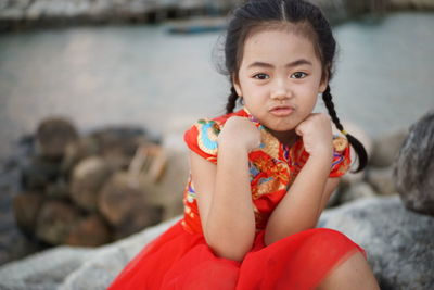 Portrait of cute girl making a face while sitting on rocks against sea