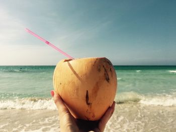 Close-up of hand holding coconut on beach