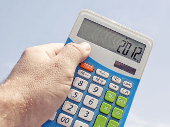 Cropped image of man holding calculator against sky