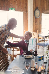 Senior man talking with female friend holding present at table in restaurant