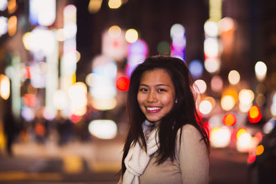 Portrait of smiling young woman standing in illuminated city