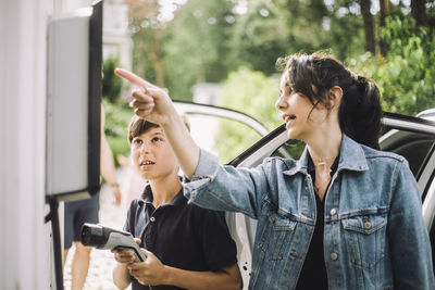 Mother pointing at charging board by son holding cable near car