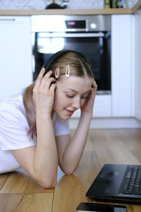 A young girl of 15-18 years old lies on the floor with a laptop and a telephone