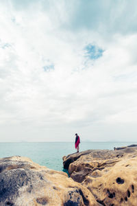 Woman standing on rock at beach against sky