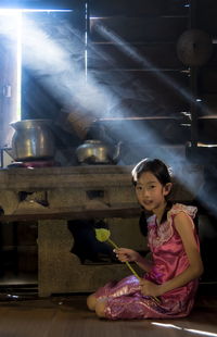 Portrait of girl holding flower bud while sitting in kitchen