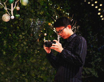 Low angle view of young man taking picture on camera by christmas tree