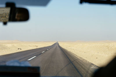 Empty road amidst desert seen through car windshield