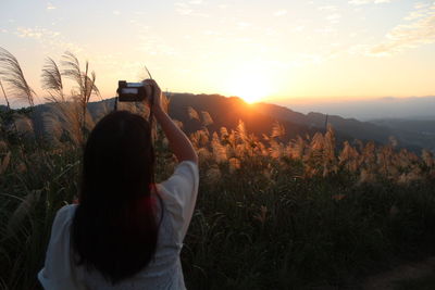 Rear view of woman photographing with camera on mountain at sunset