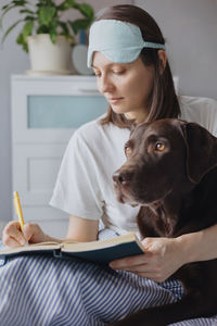 Portrait of young woman with dog sitting at home