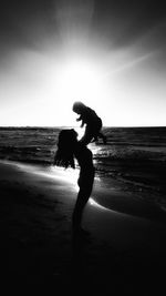 Silhouette mother holding her baby against sky at beach during sunset