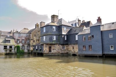 Buildings by river against sky