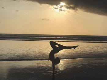 Silhouette man with arms raised on beach against sky during sunset