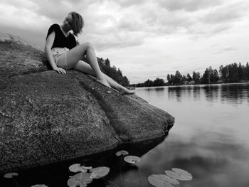 Girl sitting on rock in lake against sky
