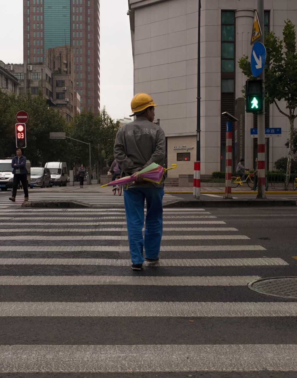 REAR VIEW OF MAN WALKING ON ROAD IN CITY