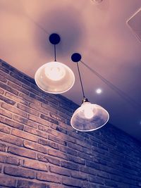 Low angle view of illuminated light bulb hanging on wall