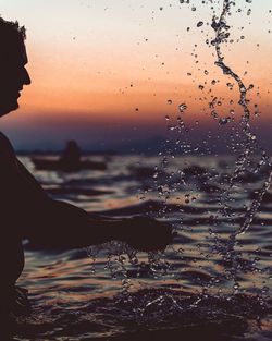 Close-up of silhouette man against sea during sunset