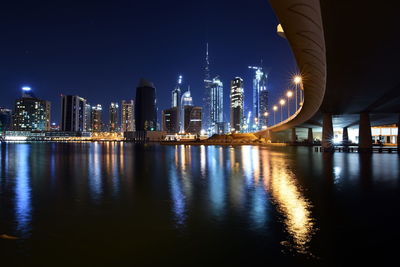 Illuminated buildings by river against sky at night