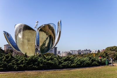 Plants against trees and building against clear blue sky