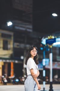 Portrait of woman standing on illuminated street at night