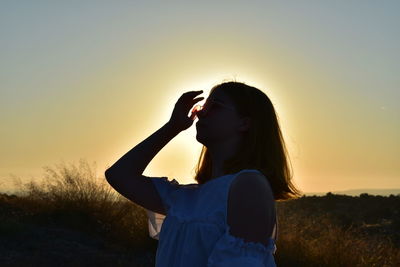 Beautiful woman standing on field against sky during sunset