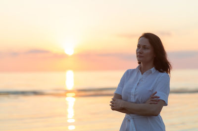 Portrait of young woman standing against sea during sunset