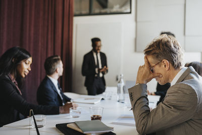 Side view of businessman with head in hand during meeting with colleagues in board room at office