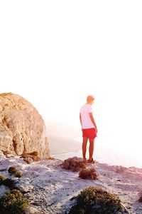 Rear view of young woman standing on rock by sea against clear sky