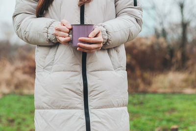 A girl in a jacket holds a purple mug with hot tea. drink a warm drink outdoors. atmospheric frame.