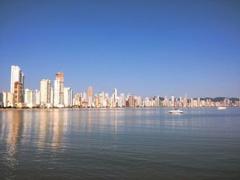 Sea by cityscape against clear blue sky