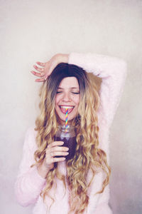 Smiling woman drinking smoothie against wall