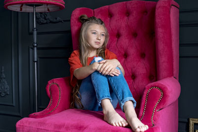 Full length of girl sitting on sofa at home