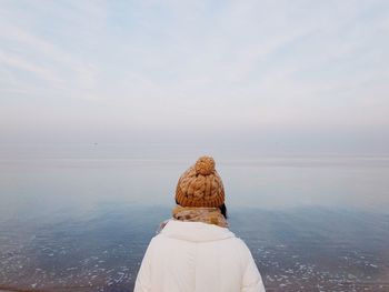 Rear view of woman standing at beach against sky