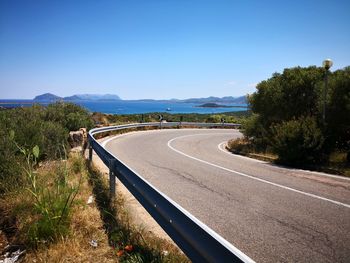 Road leading towards mountains against clear blue sky