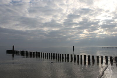 Wooden posts in sea against sky