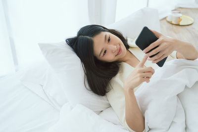 Young woman using mobile phone while lying on bed at home