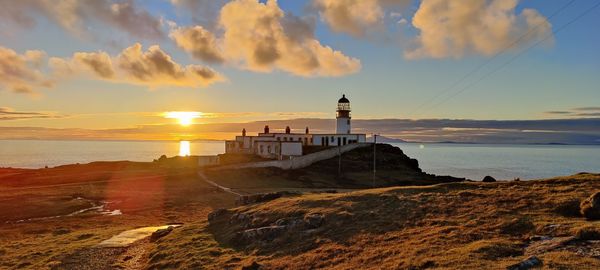 Lighthouse by sea against sky during sunset