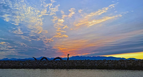 Man standing by sea against sky during sunset