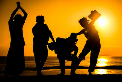 Silhouette friends at beach against sky during sunset