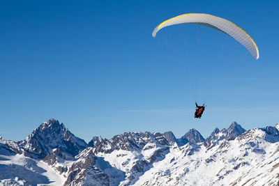 Person paragliding on snowcapped mountain against sky