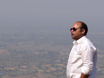 Side view of young man looking at cityscape against sky