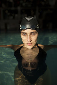 Young beautiful woman in the indoor pool, wearing black swimsuit, look at camera