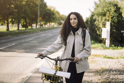 Portrait of smiling female architect wheeling bicycle on sidewalk in city