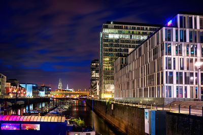 Illuminated buildings by river against sky at night