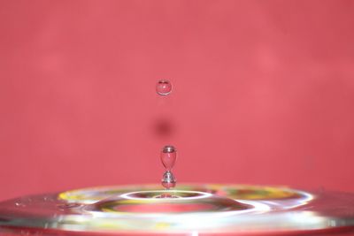 Close-up of drop falling in water against red wall