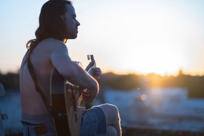 Young man playing guitar during sunset