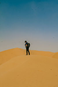 Man standing on sand dune in desert against sky