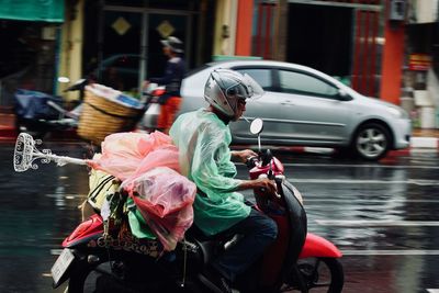 Rear view of man riding motorcycle on street during rainy season