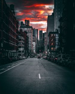 Road amidst buildings against sky during sunset