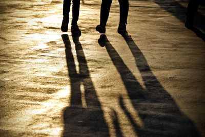 Low section of silhouette people walking on footpath during sunset