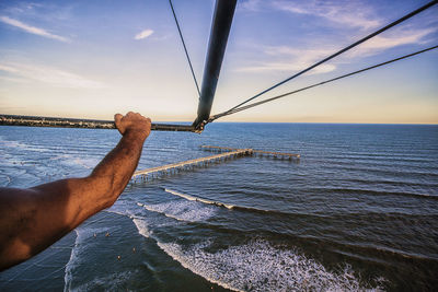 Cropped hand of man flying with hang glider over sea